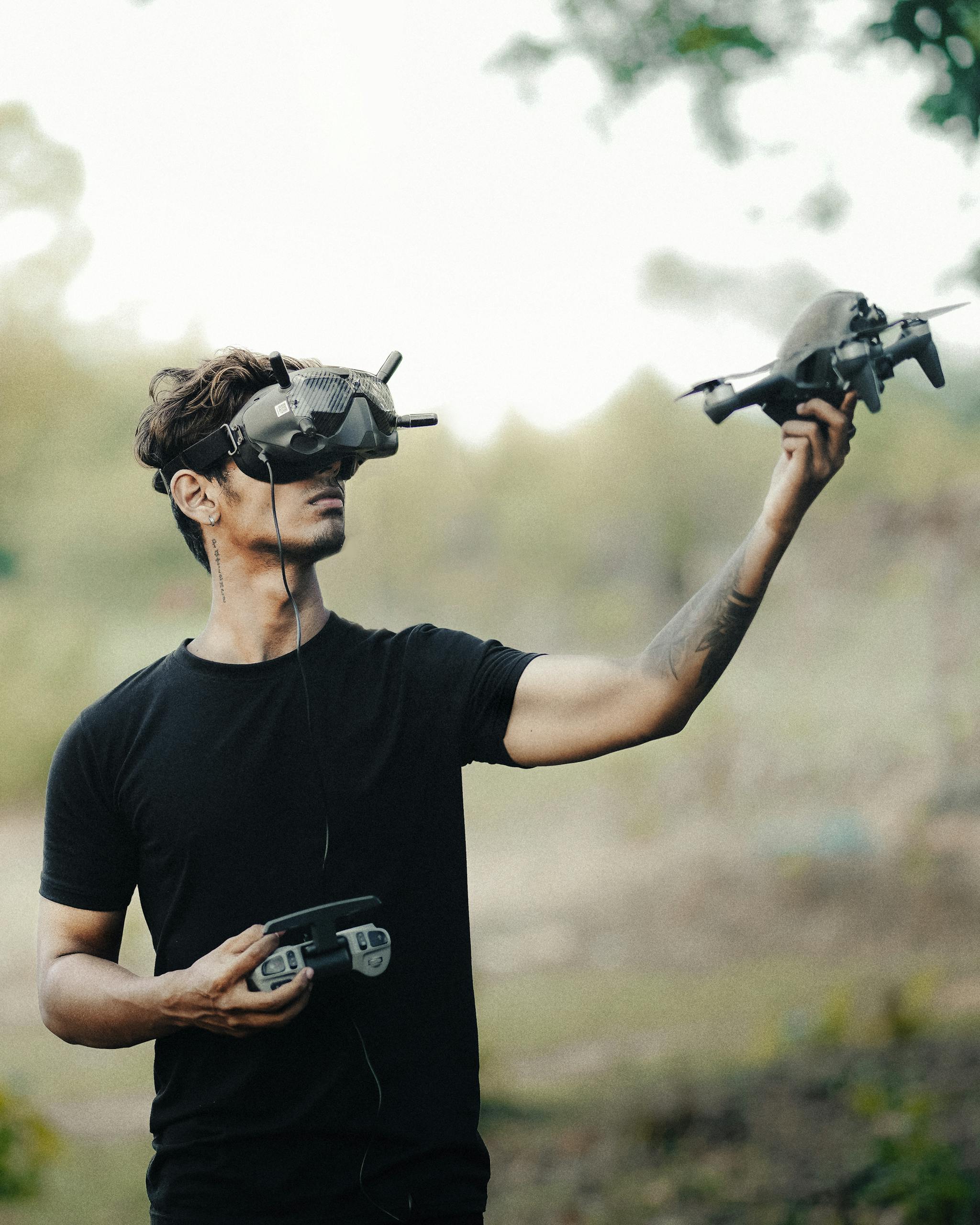 Man uses VR headset and remote to control drone in a natural setting, exploring modern technology.