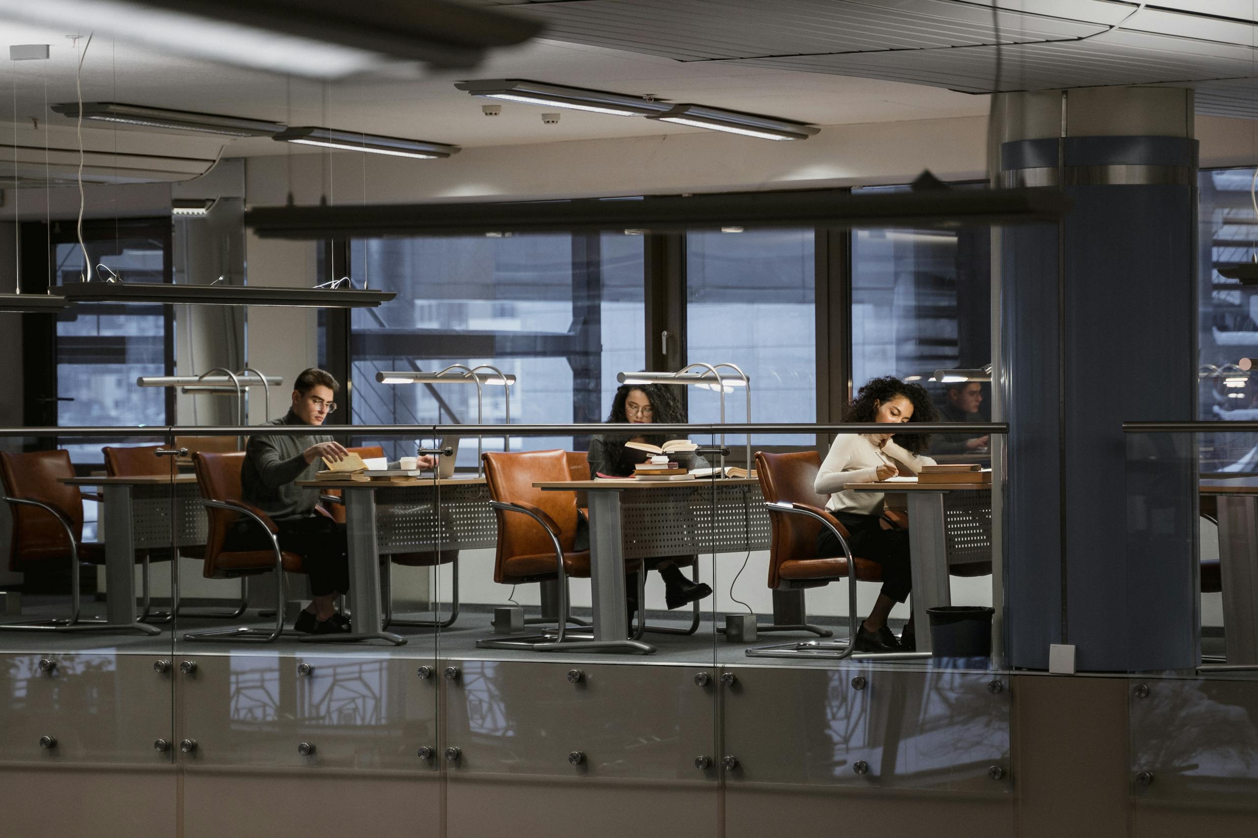 Students studying in a modern library with leather chairs and books around them.